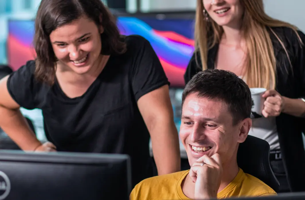 Image showing one person at a computer while two others are standing behind, offering suggestions related to design