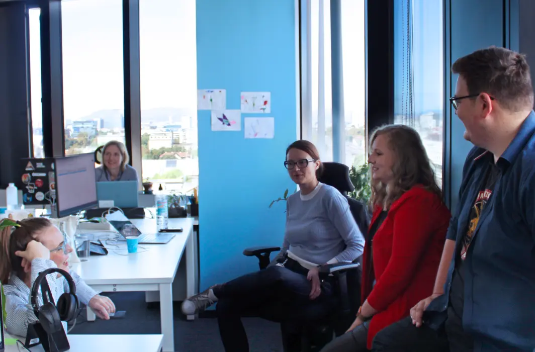 Image showing a marketing team in a relaxed atmosphere, gathered around a computer, discussing something